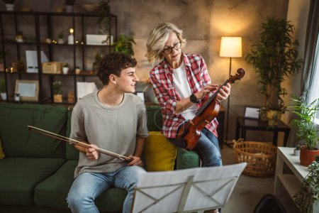 Téléchargez les photos : Jeune homme apprendre à jouer du violon sous l'instruction d'une femme mature professeur tuteur à la maison prendre des cours privés - en image libre de droit