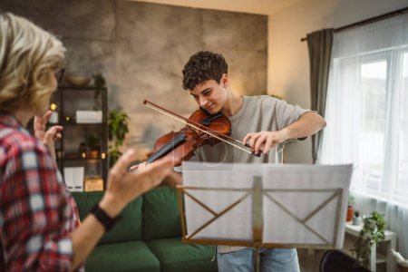 Téléchargez les photos : Jeune homme apprendre à jouer du violon sous l'instruction d'une femme mature professeur tuteur à la maison prendre des cours privés - en image libre de droit