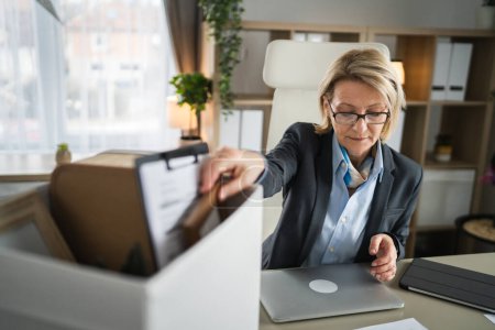 mature caucasian woman businesswoman at the office lost her job packing personal items things in box being fired from work