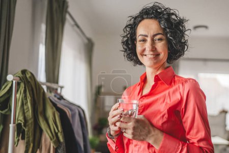 Téléchargez les photos : Portrait d'une femme adulte mature tenant un verre d'eau à la maison - en image libre de droit