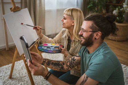 Téléchargez les photos : Couple peinture sur toile chevalet à la maison pinceau aider à apprendre à faire peinture pinceau tenir heureux homme et femme dans l'amour petit ami et petite amie ou mari et femme - en image libre de droit