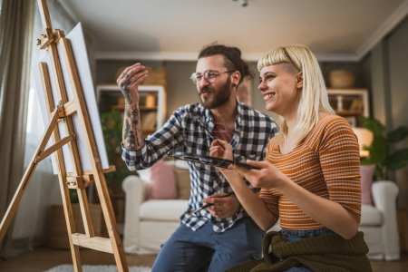 Photo for Couple paint on canvas easel at home hold brush help to learn how to do painting hold brush happy man and woman in love boyfriend and girlfriend or husband and wife - Royalty Free Image