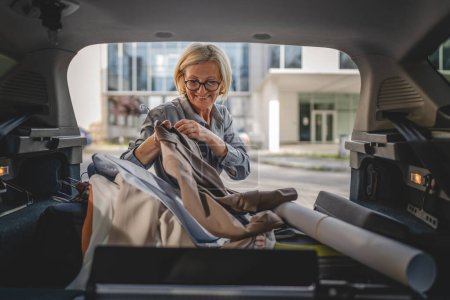 Photo for One mature blonde beautiful business woman travel concept female take stuff belongings from the back of her car while moving or arrive to destination or work real people copy space - Royalty Free Image