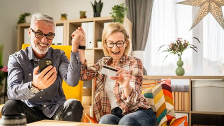 Téléchargez les photos : Mature ou senior couple mari et femme shopping en ligne assis à la maison - en image libre de droit