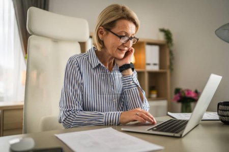 Téléchargez les photos : Mature femme d'affaires utiliser ordinateur portable au travail au bureau - en image libre de droit