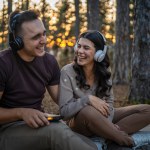 Man and woman young adult couple in nature listen music on headphones use use mobile phone smartphone or make a video call app