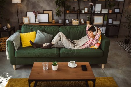 Téléchargez les photos : Femme Japonaise assise à la maison utiliser une tablette numérique pour regarder un film ou avoir un appel vidéo - en image libre de droit