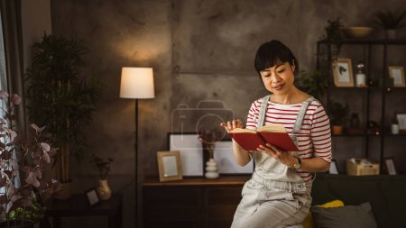 Téléchargez les photos : Une femme mature japonaise femme lire livre à la maison - en image libre de droit