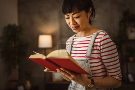Téléchargez les photos : Une femme mature japonaise femme lire livre à la maison - en image libre de droit