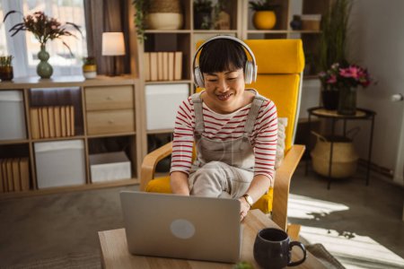 Téléchargez les photos : Femme Japonaise assise à la maison utilisation ordinateur portable pour regarder un film ou avoir un appel vidéo - en image libre de droit