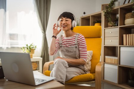 Téléchargez les photos : Femme Japonaise assise à la maison utilisation ordinateur portable pour regarder un film ou avoir un appel vidéo - en image libre de droit