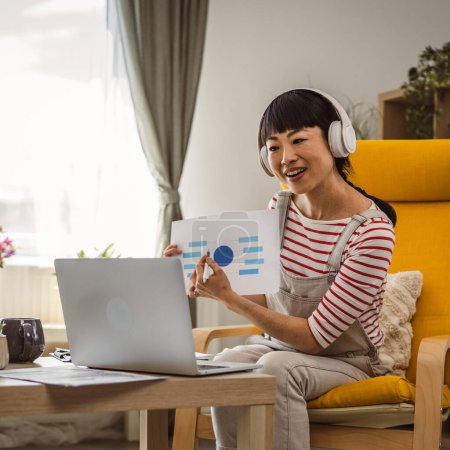 Foto de Mujer madura mujer de negocios japonesa tienen videollamada uso portátil trabajo desde casa consulta en línea o conferencia mostrar oferta de contrato de documento en papel o estadísticas - Imagen libre de derechos