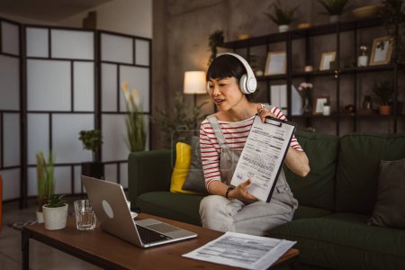 Foto de Mujer madura mujer de negocios japonesa tienen videollamada uso portátil trabajo desde casa consulta en línea o conferencia mostrar oferta de contrato de documento en papel o estadísticas - Imagen libre de derechos