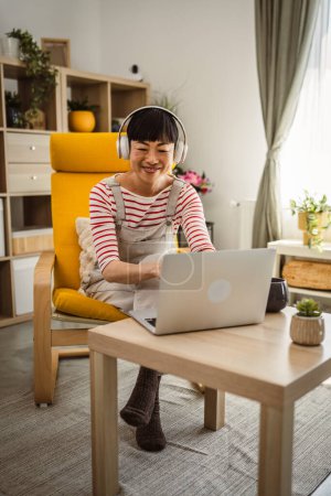 Téléchargez les photos : Femme japonaise travailler à la maison à l'ordinateur portable et détenir un document - en image libre de droit