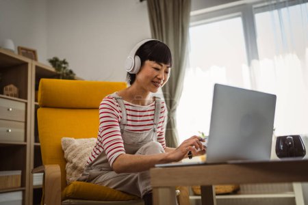 Photo for Japanese woman work at home at laptop and hold document - Royalty Free Image
