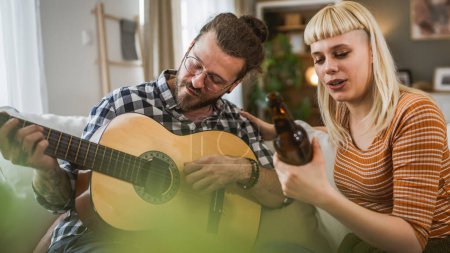 Téléchargez les photos : Couple adulte profiter à la maison jouer de la guitare et boire de la bière heureux ensemble - en image libre de droit