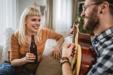 Photo for Adult couple enjoy at home play guitar and drink beer happy together - Royalty Free Image