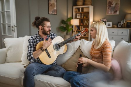 Téléchargez les photos : Couple adulte profiter à la maison jouer de la guitare et boire de la bière heureux ensemble - en image libre de droit