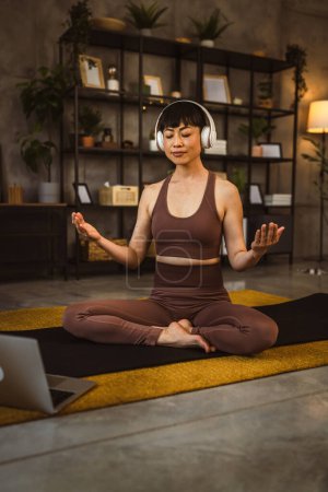 One japanese woman on the floor at home practice yoga online guided meditation with headphones on her head use laptop computer