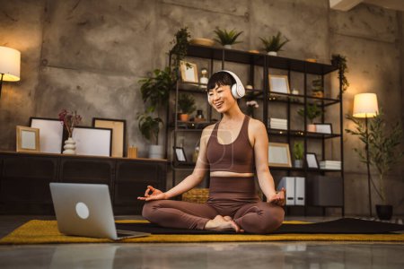 One japanese woman on the floor at home practice yoga online guided meditation with headphones on her head use laptop computer