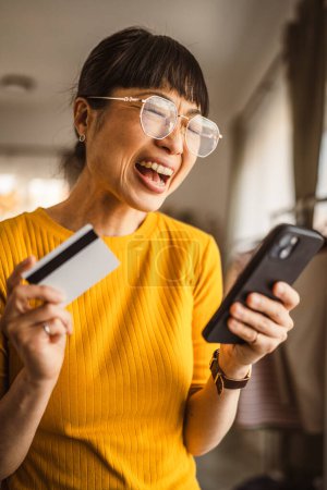 Foto de Japonesa madura mujer comprar en línea con teléfono móvil y tarjeta de crédito en casa - Imagen libre de derechos