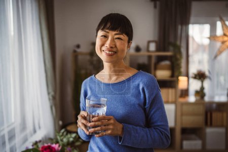 Téléchargez les photos : Portrait of one japanese mature woman with glass of water at home - en image libre de droit