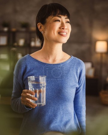 Téléchargez les photos : Portrait d'une femme mûre japonaise avec verre d'eau à la maison - en image libre de droit