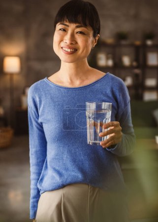 Téléchargez les photos : Portrait d'une femme mûre japonaise avec verre d'eau à la maison - en image libre de droit