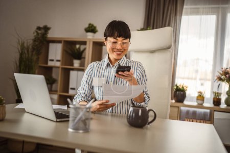Foto de Madura japonesa mujer de negocios con anteojos sentarse y escanear documento en la oficina sonrisa, feliz - Imagen libre de derechos