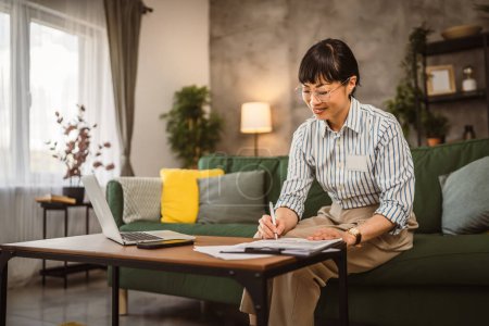 Téléchargez les photos : Femme japonaise mature avec des lunettes de travail de la maison et signer le document - en image libre de droit