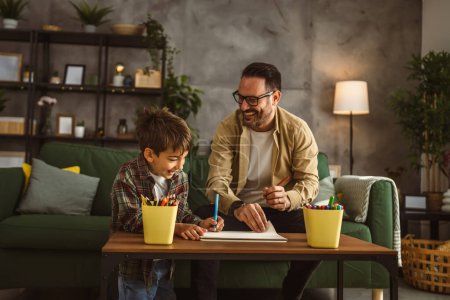 Téléchargez les photos : Père avec des lunettes et fils caucasien dessiner et peindre ensemble à la maison loisirs - en image libre de droit