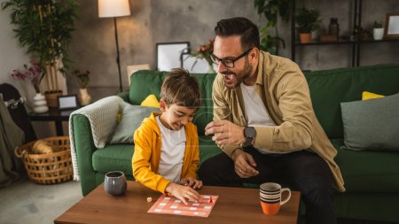 Photo for Father with eyeglasses and son caucasian play board game together at home happy enjoy - Royalty Free Image
