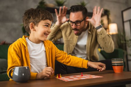Foto de Padre con anteojos e hijo caucásico jugar juego de mesa juntos en casa feliz disfrutar - Imagen libre de derechos