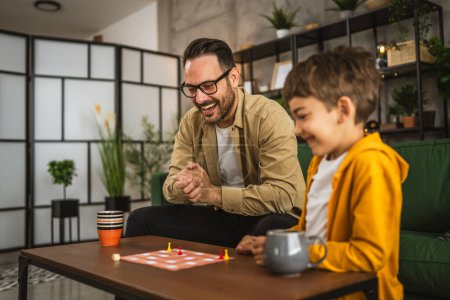 Foto de Padre con anteojos e hijo caucásico jugar juego de mesa juntos en casa feliz disfrutar - Imagen libre de derechos