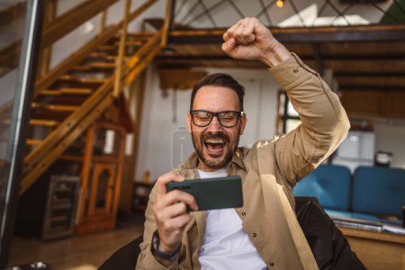 Téléchargez les photos : Adult caucasian with eyeglasses man play video games on his phone at home - en image libre de droit