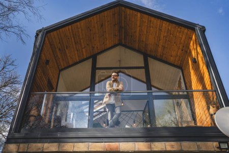 Photo for Adult caucasian man with eyeglasses stand on the balcony and look into the distance - Royalty Free Image