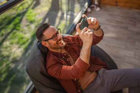 Photo for Adult caucasian with eyeglasses man play video games on his phone at home - Royalty Free Image