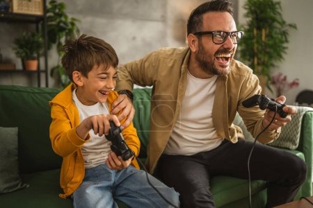 Téléchargez les photos : Père et fils caucasien jouer à des jeux vidéo avec joystick et amusez-vous à la maison heureux profiter - en image libre de droit