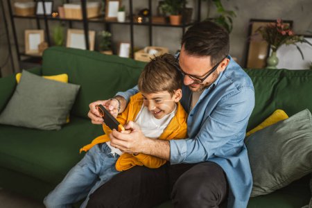 Photo for Father and son play video games on a mobile phone and enjoy at home - Royalty Free Image