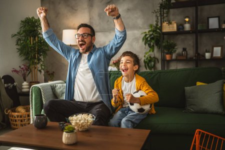 Photo for Father and son caucasian watch football match and cheer at home noisy, excited, happy - Royalty Free Image
