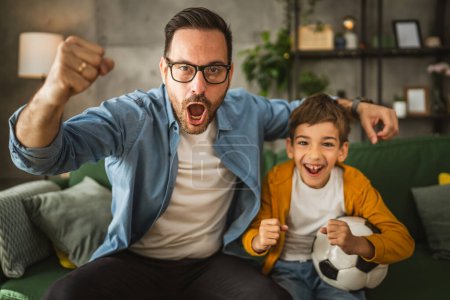 Foto de Padre e hijo caucásico ver partido de fútbol y alegría en casa ruidoso, emocionado, feliz - Imagen libre de derechos