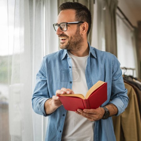Porträt eines erwachsenen kaukasischen Mannes mit Brille lesen Buch im Wohnzimmer glücklich und entspannen