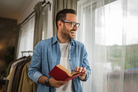 Porträt eines erwachsenen kaukasischen Mannes mit Brille lesen Buch im Wohnzimmer glücklich und entspannen