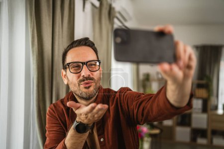 Portrait of adult caucasian man take a self portrait and send kiss at home