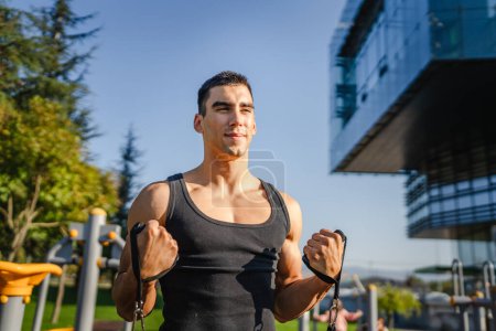 Téléchargez les photos : Homme caucasien adulte s'entraînant en plein air dans la journée de la ville Athlète masculin utilisant des tubes élastiques en caoutchouc de bande de résistance dans sa routine d'entraînement quotidienne - en image libre de droit