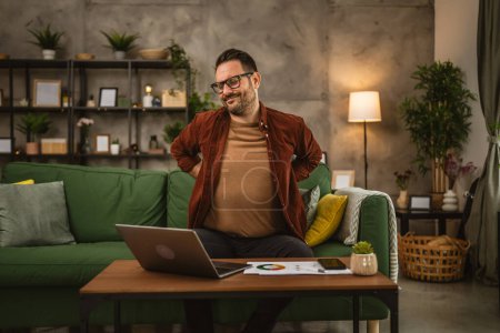 Photo for Exhausted adult man have back or kidney pain while he work from home - Royalty Free Image