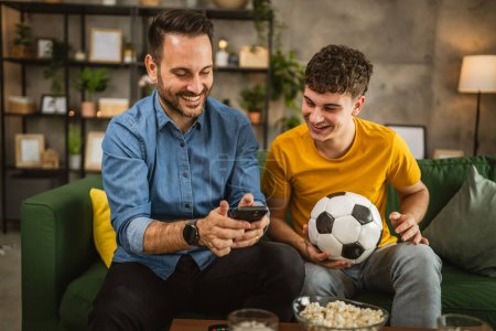 Two male friends follow football match results on mobile phone at home