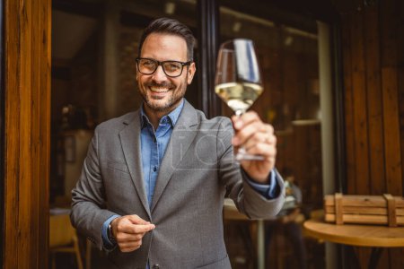 Portrait of adult man sommelier stand in front of winery and hold wine