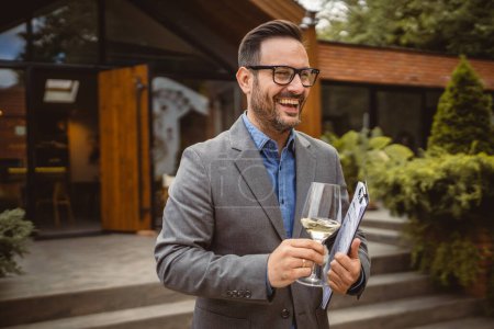 Portrait of adult man stand in front of winery hold wine and clipboard