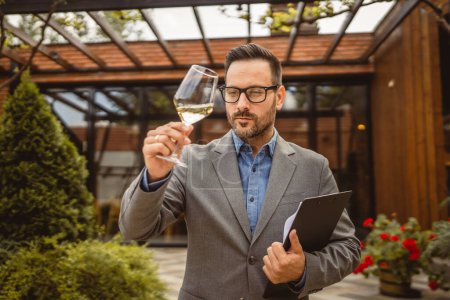 Portrait of adult man stand in front of winery hold wine and clipboard